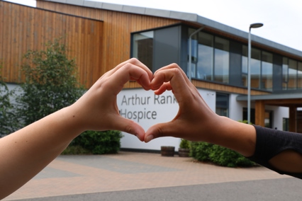 Two hands making a heart around the Arthur Rank Hospice Charity sign